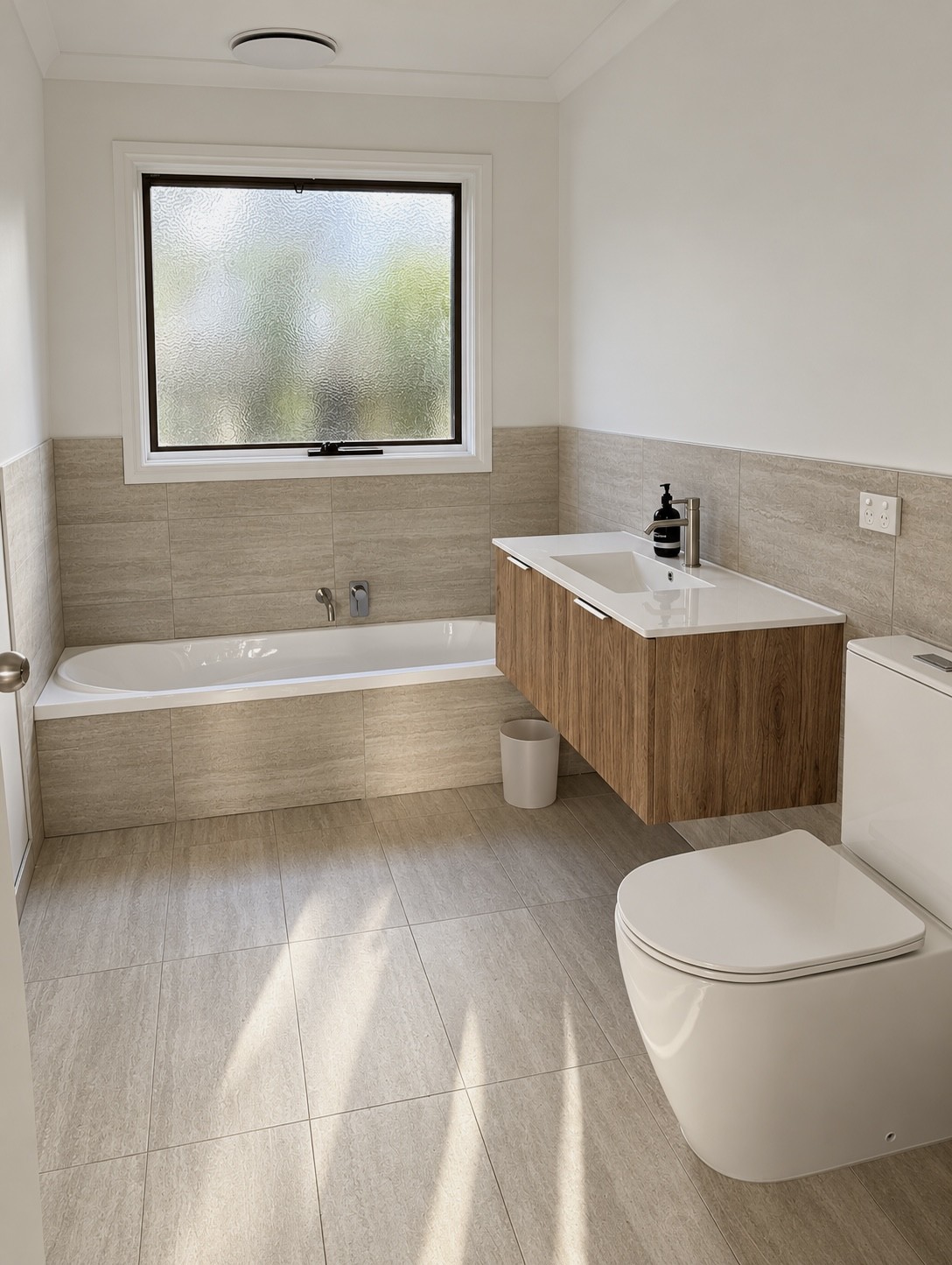 Completed bathroom with beige floor and wall tiles, built-in bath, timber vanity and toilet