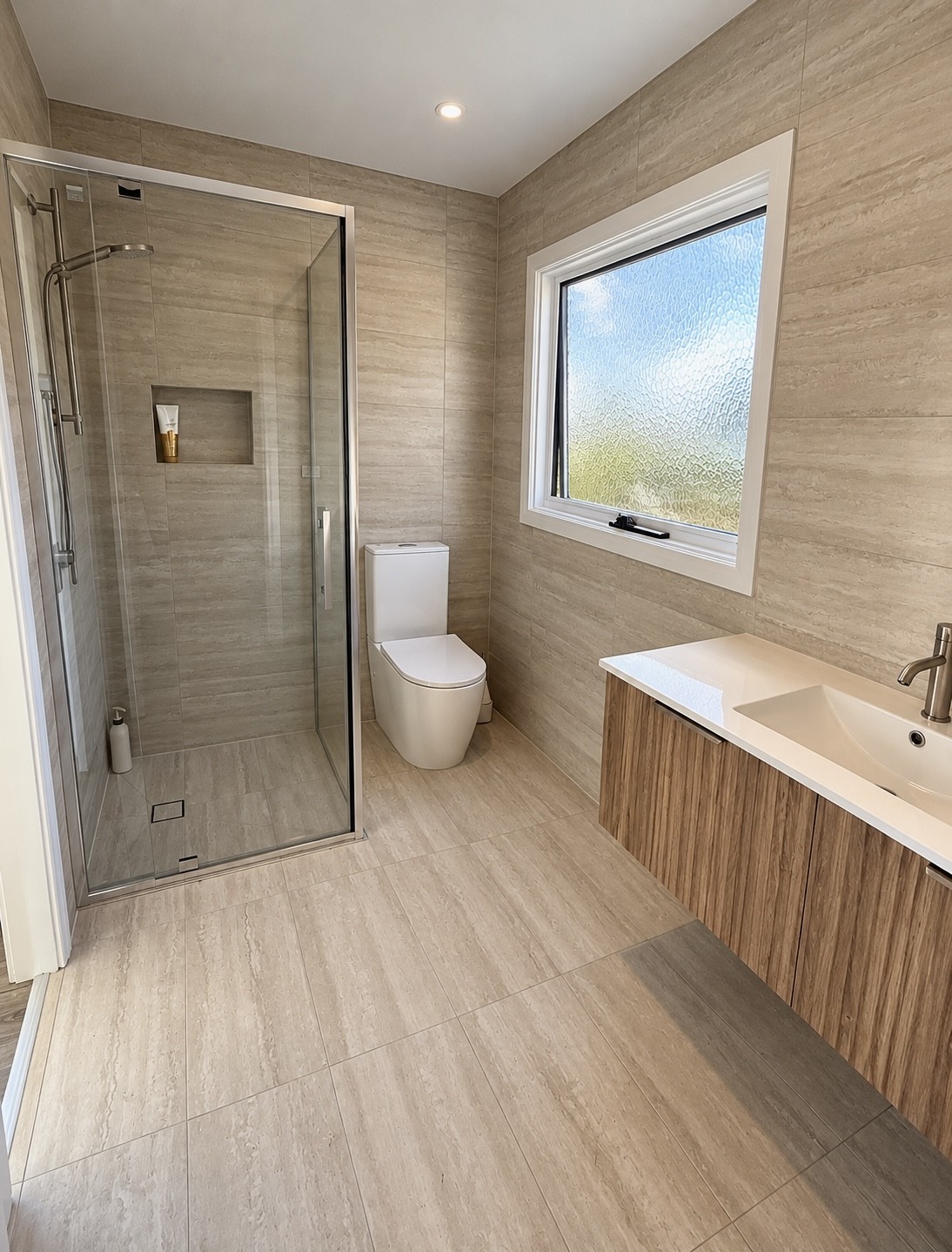 Completed bathroom with beige tiling, glass shower, timber vanity and frosted window