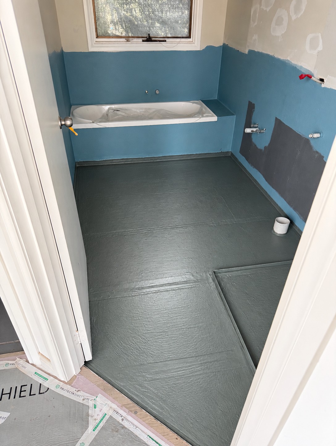Bathroom during waterproofing: blue wall membrane and dark waterproofed floor